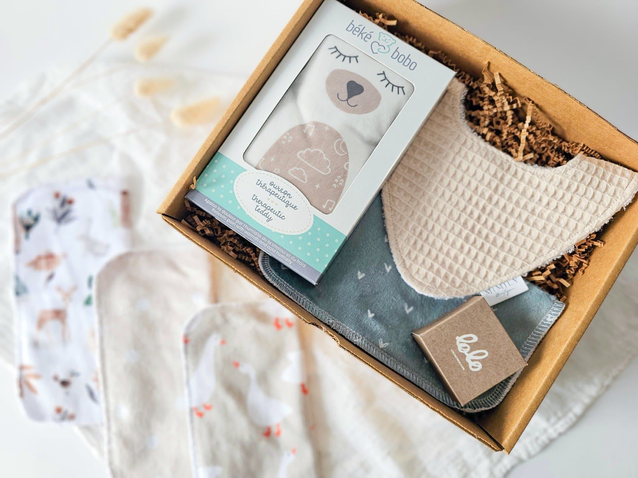 Boîte cadeau Petit trésor pour nouveau-né avec ourson thérapeutique chaud-froid Béké bobo, débarbouillette minky, bavoir absorbant et savon de Castille à l’huile d’olive, une attention douce et pratique pour bébé et nouveaux parents.